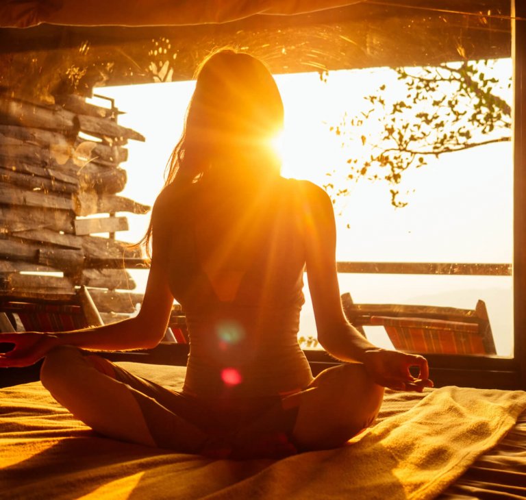woman sun rays in the form of chakras in tropical yoga studio a woman sun rays in the form of chakras in tropical yoga studio a view outside to the hills while sunset.girl in eco hotel panoramic windows enjoying solitude with nature Kerala India wildernest resort